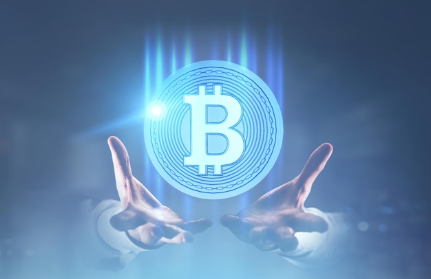 Руки неузнаваемого бизнесмена держат круглую биткойн-голограмму. Размытый синий фон. Тонированное изображение с двойной экспозицией макет.
