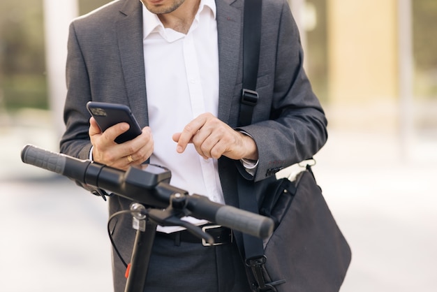 Unrecognizable businessman in suit is coming up to an electric scooter phone application for rental