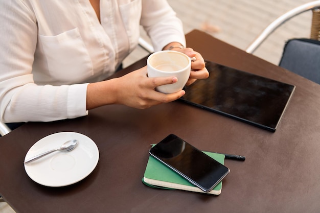 一杯のコーヒーを飲み、電話やタブレットで作業している認識できない実業家、デジタル起業家と都会のライフスタイルの概念