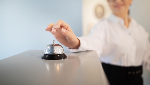 Photo unrecognizable businesswoman pushing call bell at reception counter standing indoors