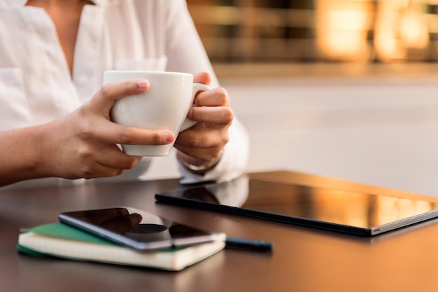 Unrecognizable businesswoman working and drinking a cup of coffee on a terrace in the city, concept of digital entrepreneur and urban lifestyle, copy space for text