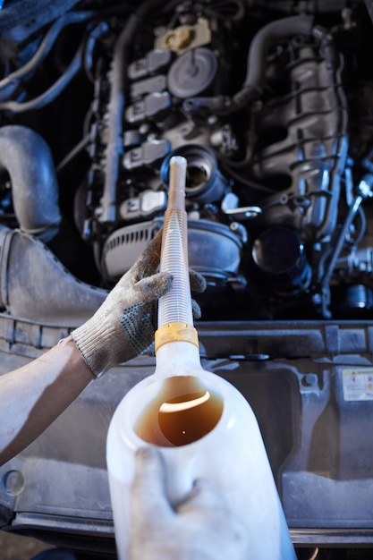 Meccanico di automobile irriconoscibile cambio olio nel motore in officina di riparazione auto, spazio di copia