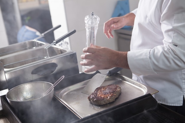 Unrecognizable chef salting rib eye grilled steak