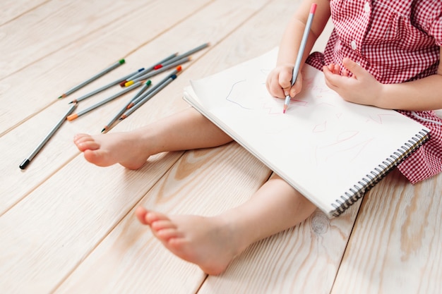 Unrecognizable child girl drawing on paper with colorful pencils.