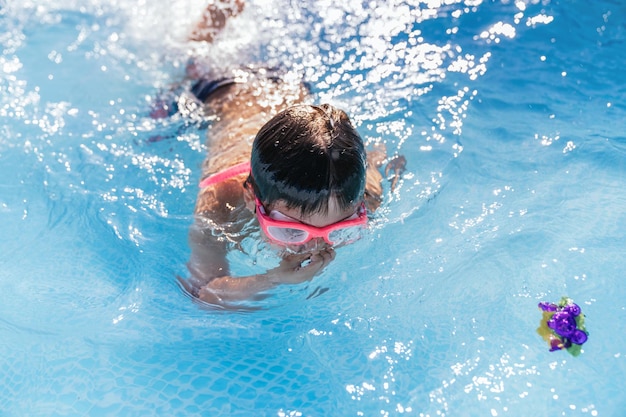 Unrecognizable child playing in a small removable pool swimming in the water