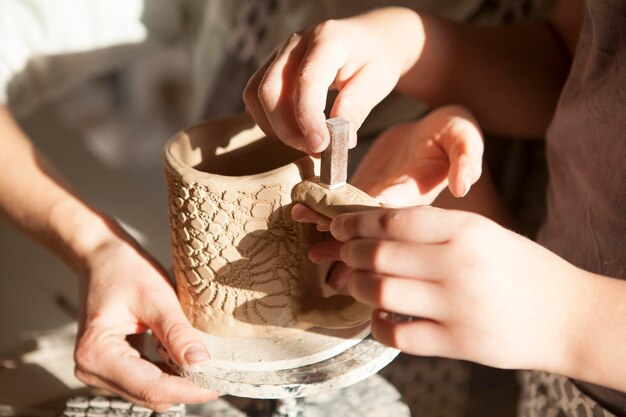 Unrecognizable child putting stamps onto clay cup at pottery\
workshop