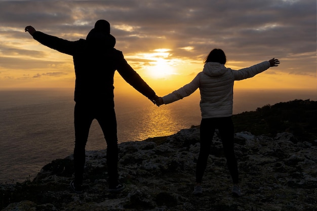 Unrecognizable couple holding hands on the Dingli Cliffs at sunset