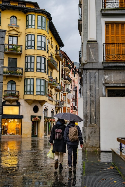 알아볼 수 없는 커플이 비를 맞으며 관광 도시의 중심을 산책하고 있습니다.