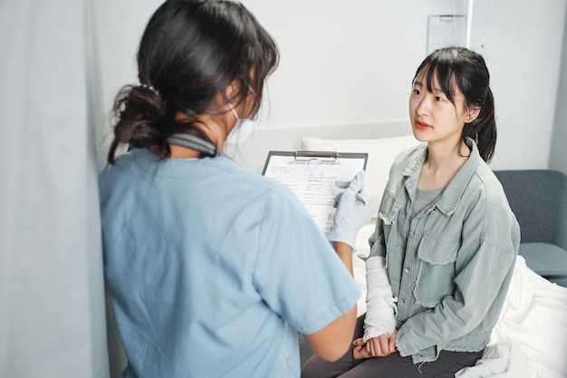 Photo unrecognizable doctor wearing mask holding clipboard with medical card asking questions to young asian woman