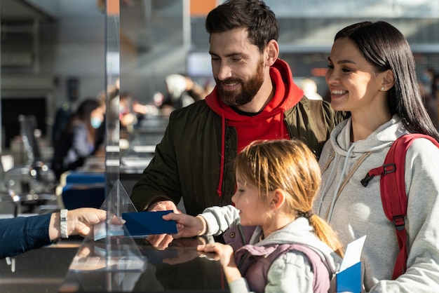 Impiegato irriconoscibile dell'aeroporto che controlla passaporti e dati biometrici mentre lavora con la famiglia dei passeggeri. genitori felici e la loro figlia che hanno viaggio