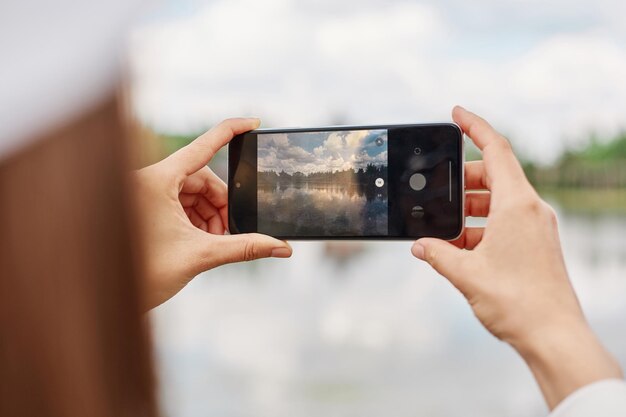 Foto irriconoscibile blogger femminile che utilizza la tecnologia cellulare per la ripresa di contenuti video durante le vacanze di viaggio donna con dispositivo smartphone che fotografa lago o fiume