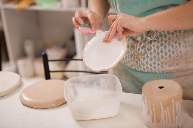 写真 彼女の陶器工房で働いている、認識できない女性の陶芸家が小さな粘土板をグレージングしている