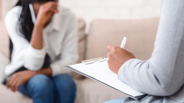 Unrecognizable female psychologist noting problems of woman patient at therapy session