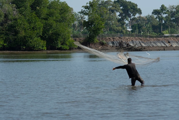 unrecognizable fisherman from the distance shore throwing fishing net to catch fish