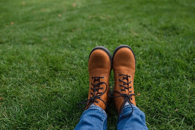 An unrecognizable girl in boots on a green lawn