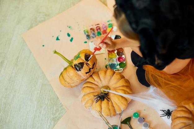 Unrecognizable girl decorating an orange pumpkin, drawing face Jack-O-Lantern for Halloween