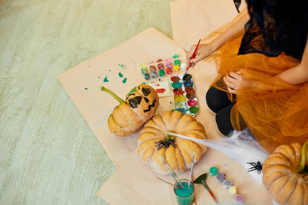 Неузнаваемая девушка, украшающая оранжевую тыкву, рисует лицо JackOLantern на Хэллоуин