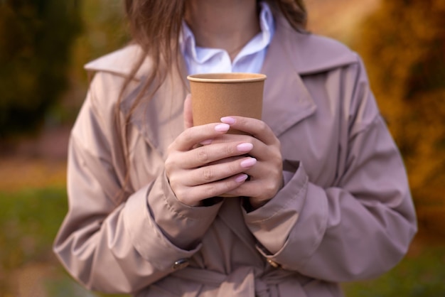 Unrecognizable girl holding cup of hot drink mockup paper cup in woman hand outdoors