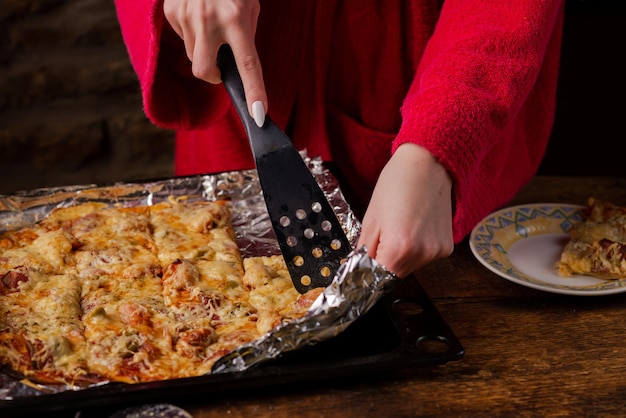 Unrecognizable girl takes piece of homemade pizza Woman's hand with long nails holds kitchen spatula
