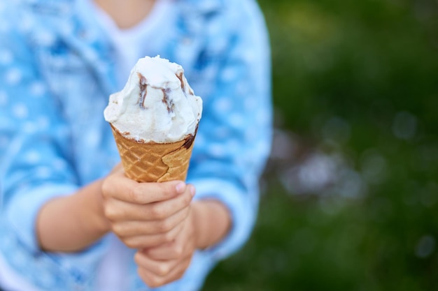 여름날 공원에서 쉬고 있는 이탈리아 아이스크림 콘을 들고 있는 알아볼 수 없는 소녀는 여름에 야외에서 아이스크림을 즐기고 있습니다.