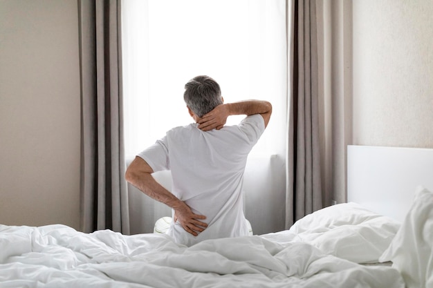 Photo unrecognizable greyhaired man sittting on bed touching back and neck