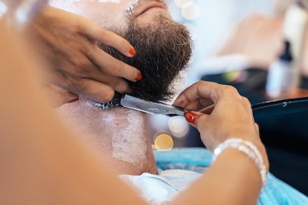 Unrecognizable hairdresser shaving a client with a manual razor