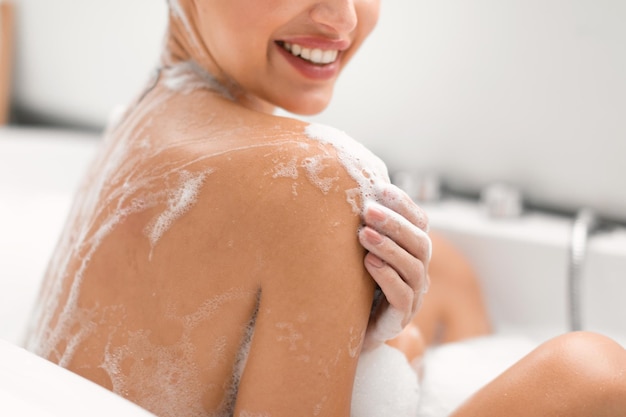 Unrecognizable lady washing body taking bath in modern bathroom cropped