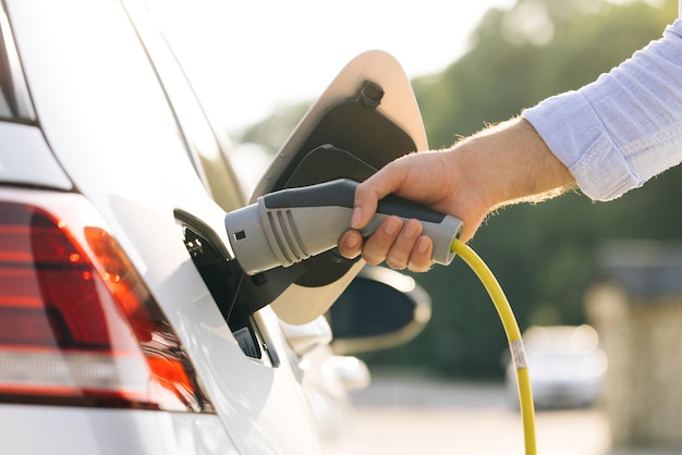 Unrecognizable man attaching power cable to electric car electric vehicle recharging battery