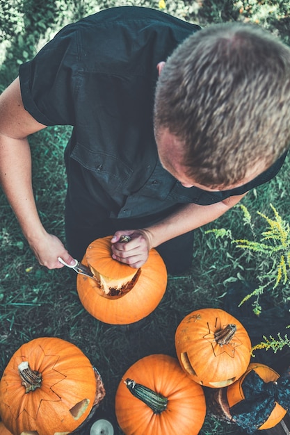 Unrecognizable man cuts a lid from a pumpkin as he prepares a jack-o-lantern.