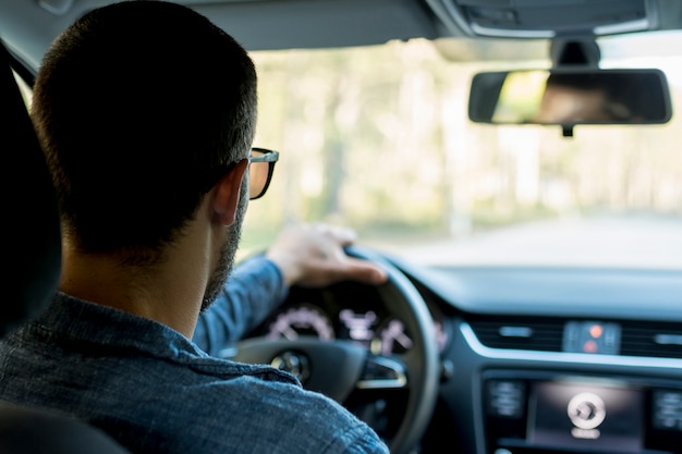 Unrecognizable man driving car on empty road