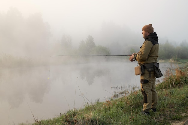 Неузнаваемый мужчина ловит рыбу в озере на рассвете