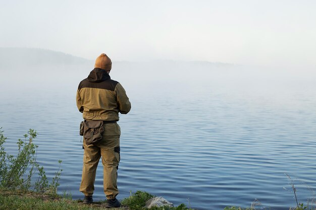 夜明けに湖で釣りをしている認識できない男