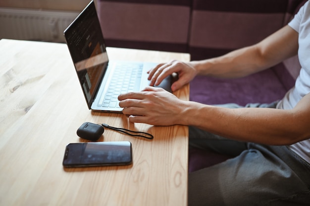 Unrecognizable man hands with smartphone and headphones working on a laptop