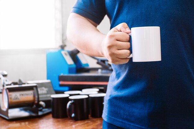 Unrecognizable man holding awhite cup behind a bottom where there are cups