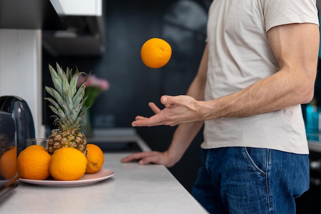 Unrecognizable man holding orange standing i in kitchen