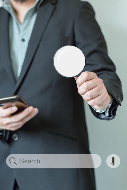 Фото Неузнаваемый мужчина в костюме с увеличительным стеклом и смартфоном для поиска в интернете