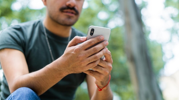 Unrecognizable man in park texting on smartphone.