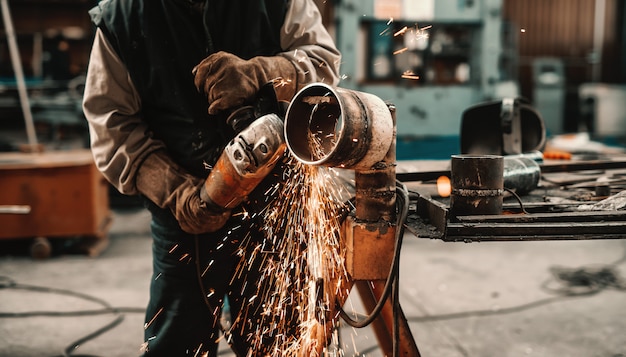 Photo unrecognizable man in protective suit and gloves cutting pipe with grinder. workshop interior.