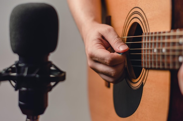 Unrecognizable man recording music with acoustic guitar and condenser microphone