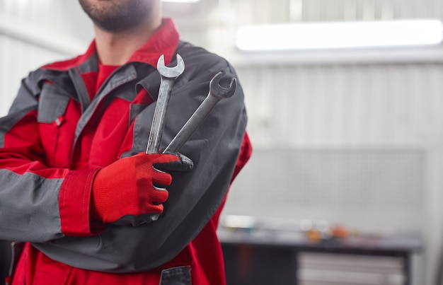 Unrecognizable man in uniform showing metal spanners and crossing arms while standing on garage during work