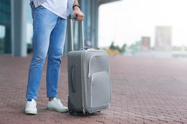 Unrecognizable Man Waiting Outside Of Airport With Suitcase