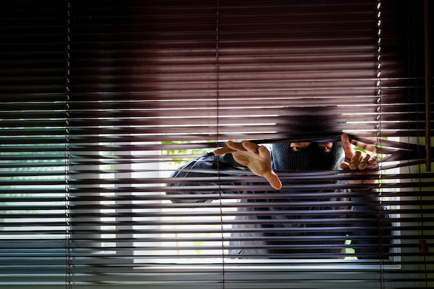 Photo unrecognizable man wearing balaclava face mask looking through venetian blind keep your home secure