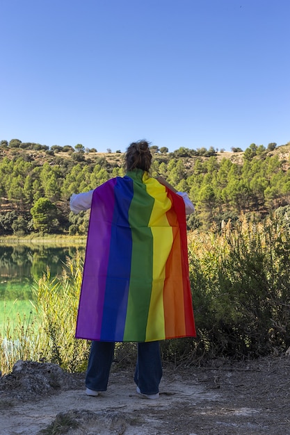 Unrecognizable middle-aged lesbian woman holding the gay rainbow flag on at the lake outdoors. freedom concept