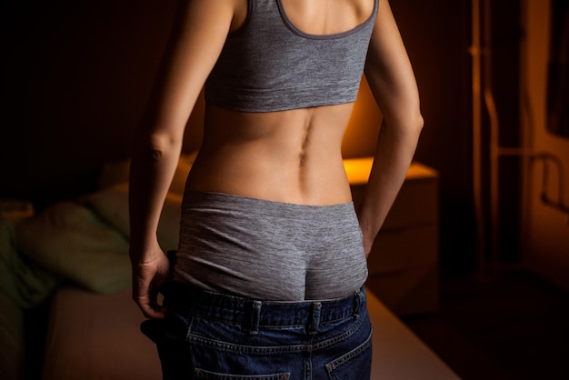 Unrecognizable middleaged woman takes off her jeans in a dark room Undress after coming home