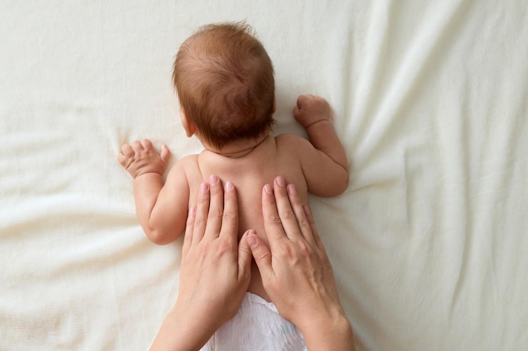 Photo unrecognizable mother doing massage for her healthy infant baby small caucasian newborn laying on his tummy while his mommy performing massage for developing muscles