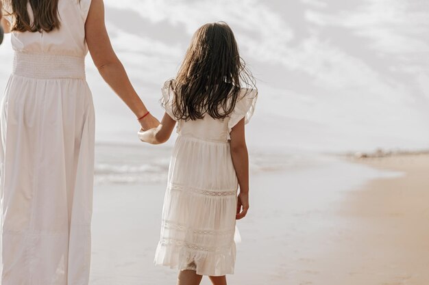 unrecognizable mother and girl holding hands on beach