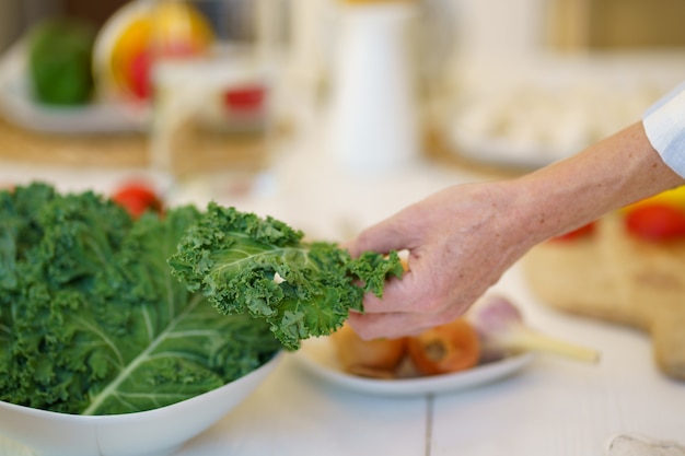 Unrecognizable old female preparing vegetable salad while cooking food in kitchen at home