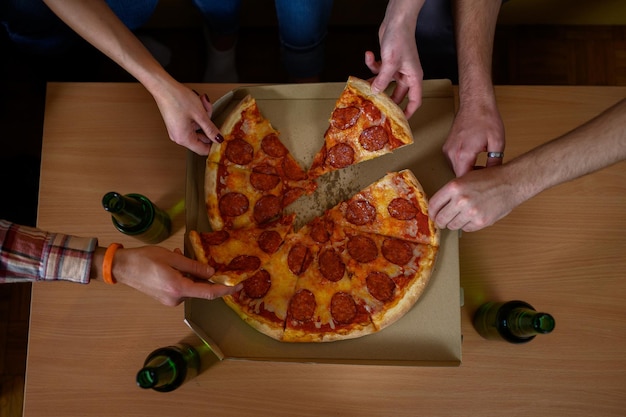 Le mani di persone irriconoscibili afferrano ciascuna una fetta di pizza