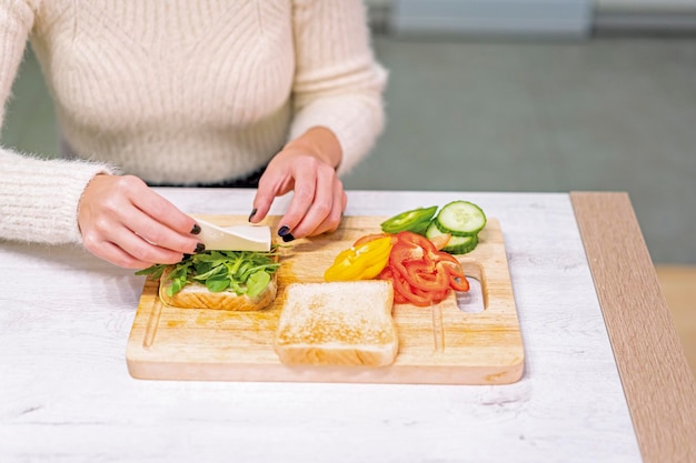 Unrecognizable person cooking a vegetable sandwich in the kitchen at home placing the cheese