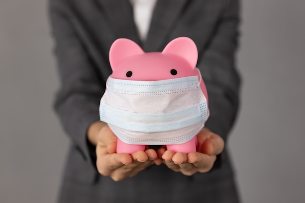 Unrecognizable person holding piggybank wearing protective mask in hands. Support business during the coronavirus pandemic concept.